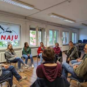 Eine kleine Menschengruppe sitzt in einem Stuhlkreis bei einem Workshop.